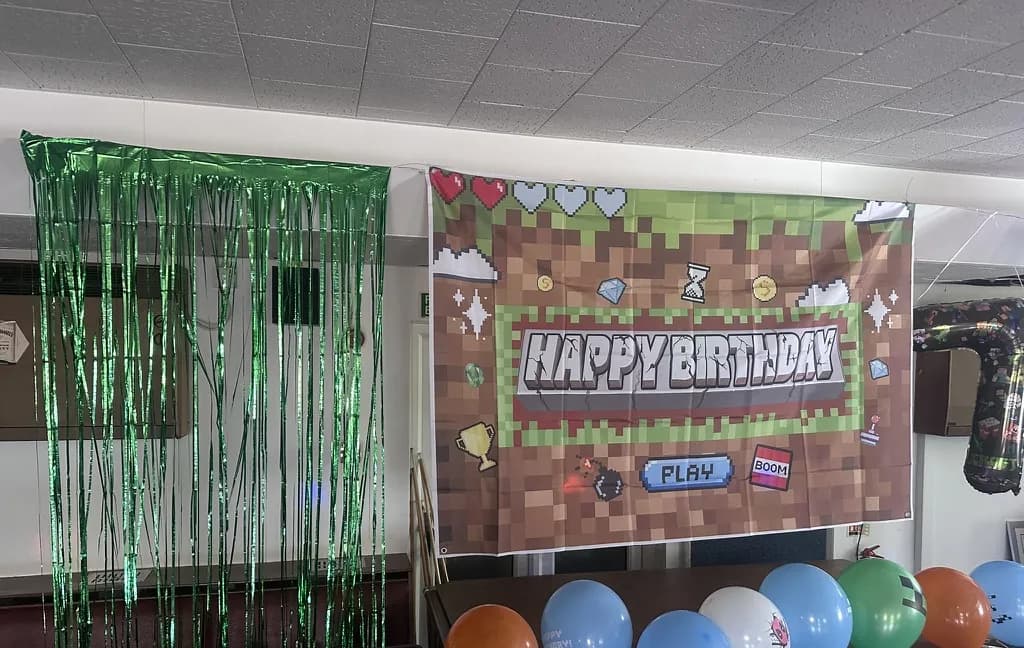 A pixel-art happy birthday backdrop and green tinsel curtain, set up for a Minecraft party in Weybridge