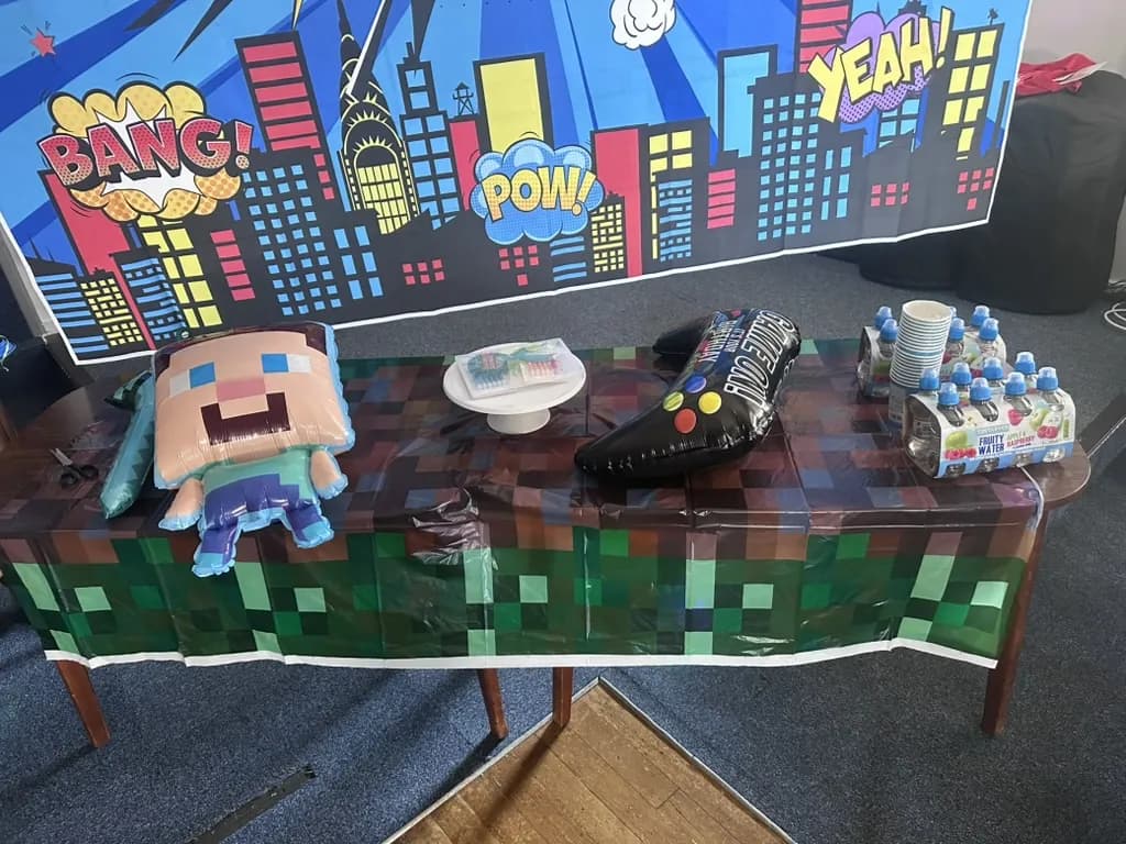 A party table in a green block tablecloth with a Steve balloon, set up for a Minecraft party in Weybridge
