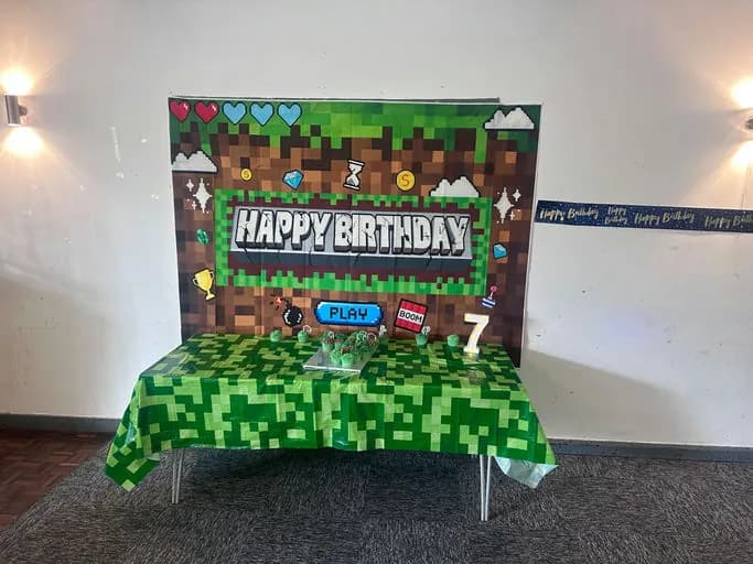 A Minecraft-themed party table in Croydon: a pixel-art happy birthday backdrop and a green block tablecloth
